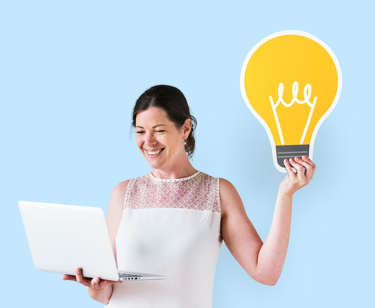 A woman holding a laptop in one hand and a cardboard light bulb illustration in the other hand
